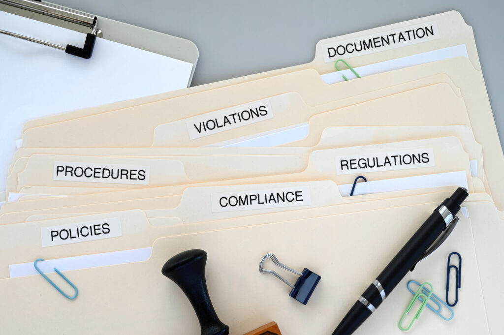 Manila file folders labeled with policies, procedures, compliance, violations, and documentation for a healthcare data privacy review