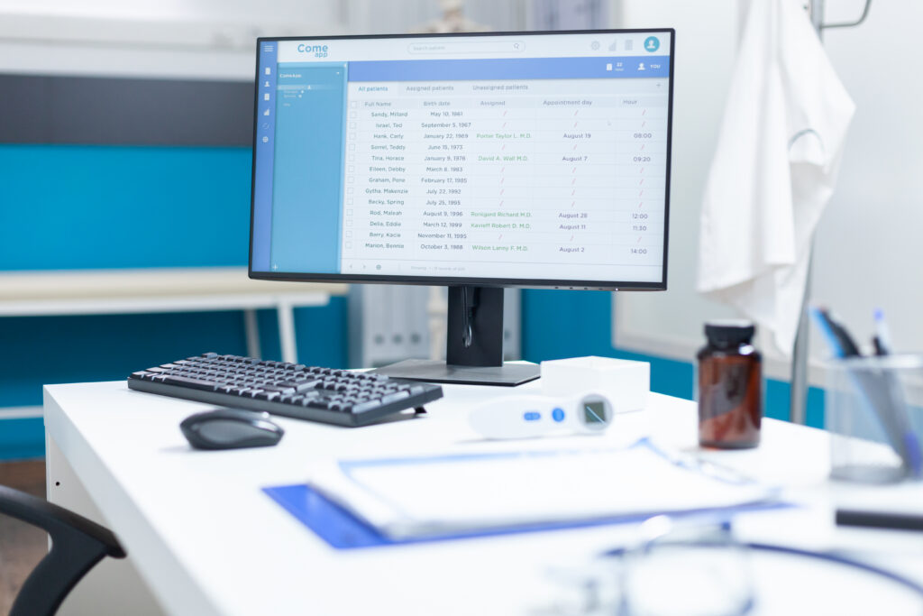 Modern medical clinic office desk featuring an EHR software screen displaying a Medicare patient panel list