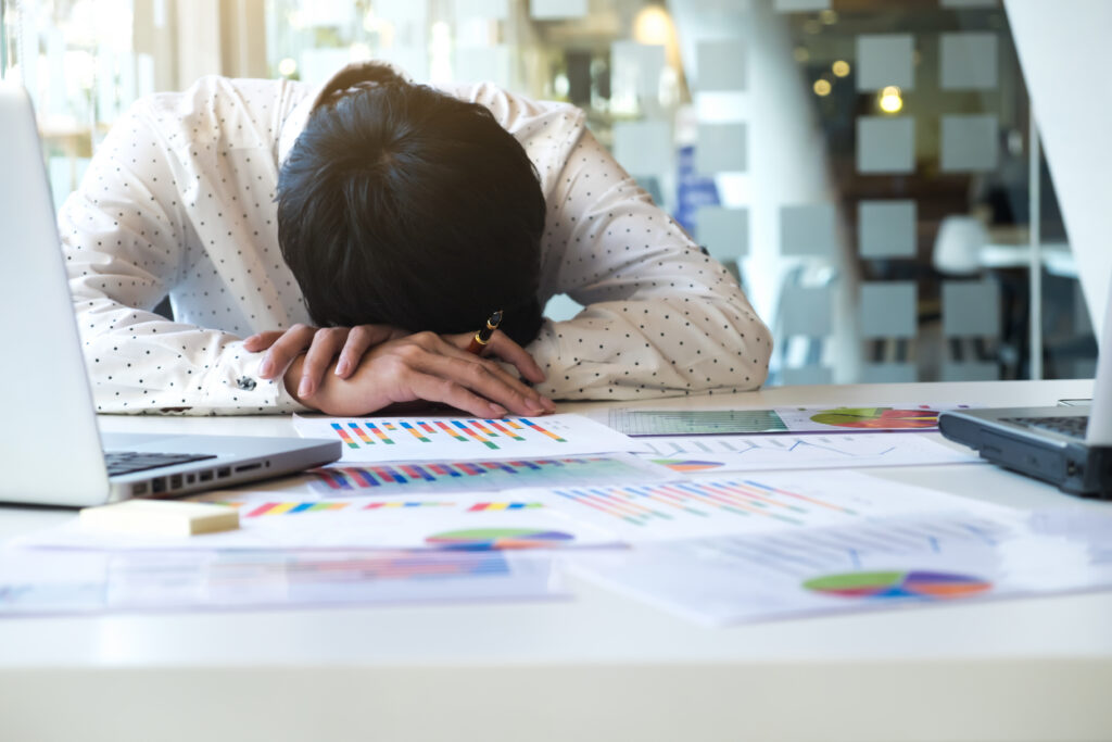 Overwhelmed clinic administrative staff member resting head on desk due to clinical workflow documentation and nurse burnout