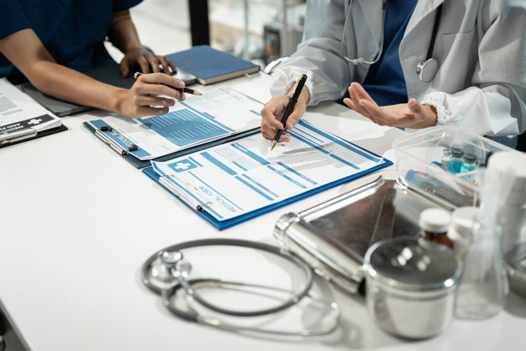 Two healthcare professionals in lab coats reviewing patient medical records and clinical documentation at a conference table