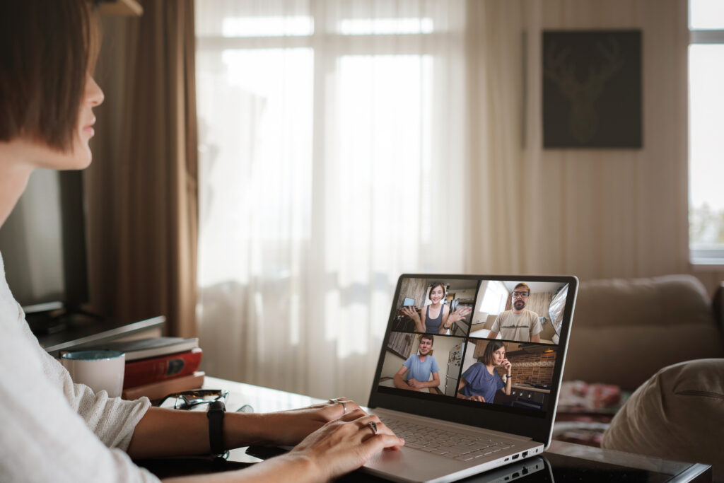 An AEC production support specialist working from home while collaborating with colleagues on a four-screen video conference call on a laptop.