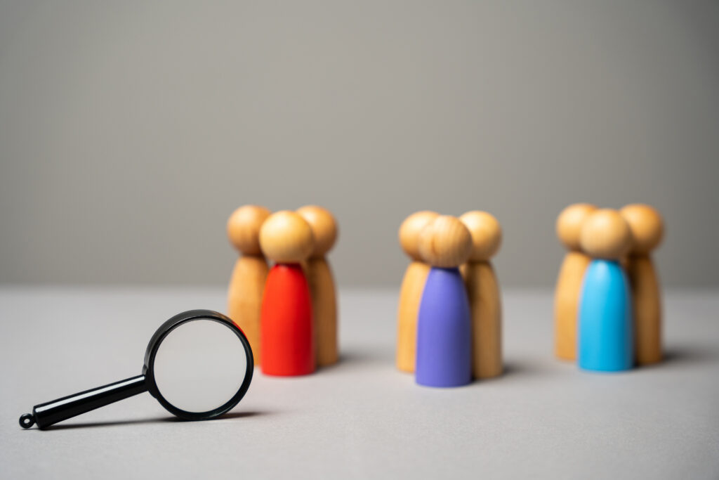 A magnifying glass focusing on segmented groups of colored wooden peg dolls, representing healthcare compliance vetting and primary source verification of healthcare providers.
