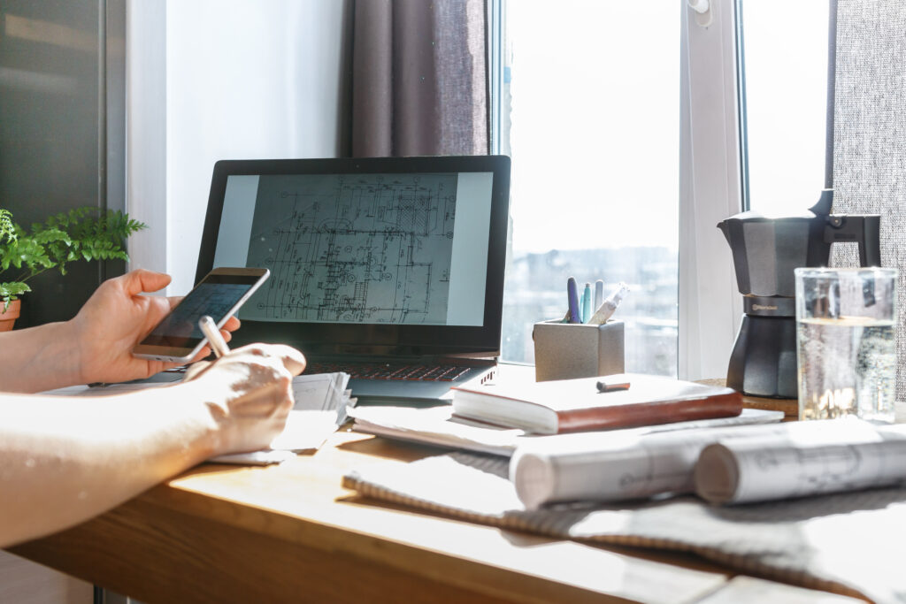 Architect reviewing a 3D 3D apartment layout model on a laptop with printed architectural blueprints on the desk.