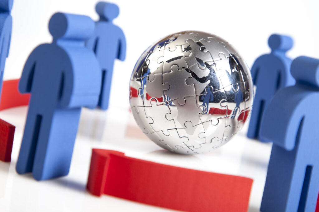 Conceptual global teamwork model showing connected figurines around a puzzle globe representing international staffing alignment