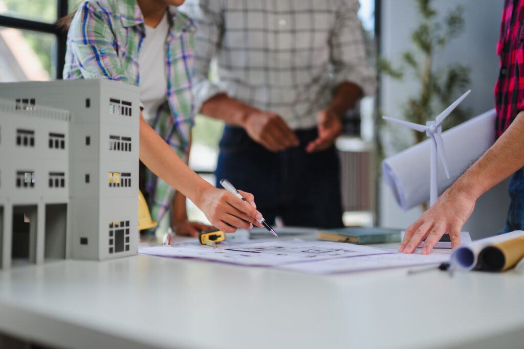 Architectural and engineering team pointing at building models and reviewing floor plans on a office desk.