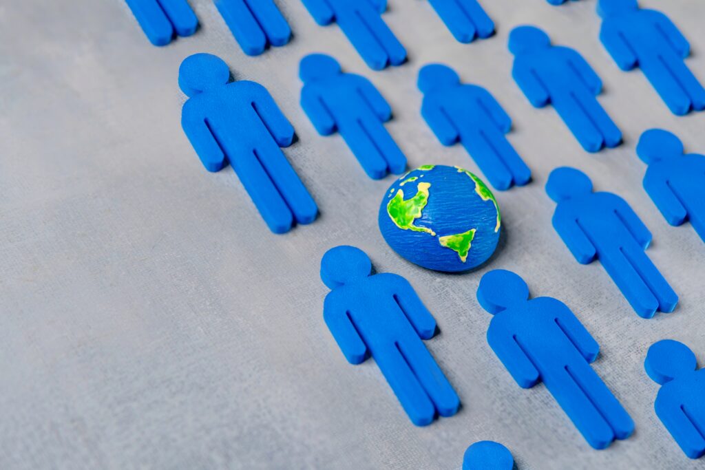 Small globe surrounded by blue human figures representing global remote talent and embedded revenue cycle staffing models.