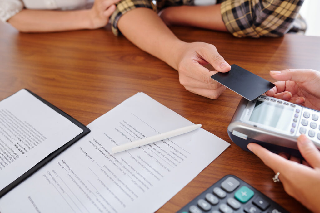 Patient tapping a credit card on a payment terminal at a clinic desk with financial documents, illustrating patient copayment collection and credit balance origins.