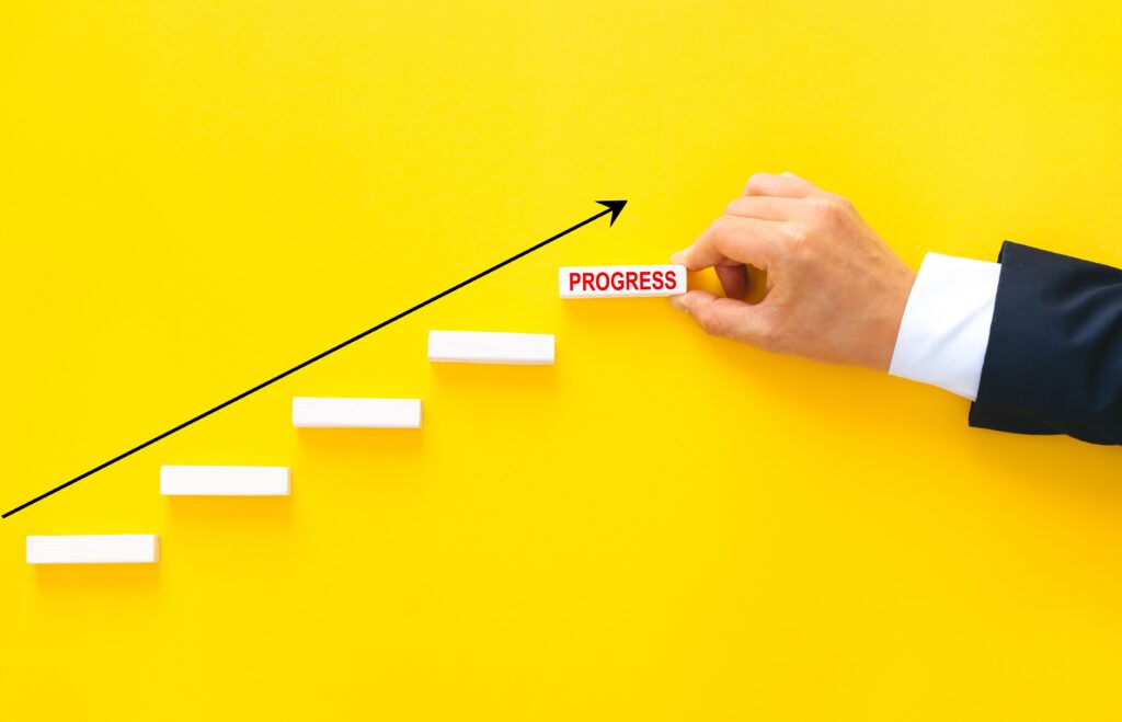 Hand placing a step block labeled progress on a rising yellow background representing AEC firm growth and strategy.