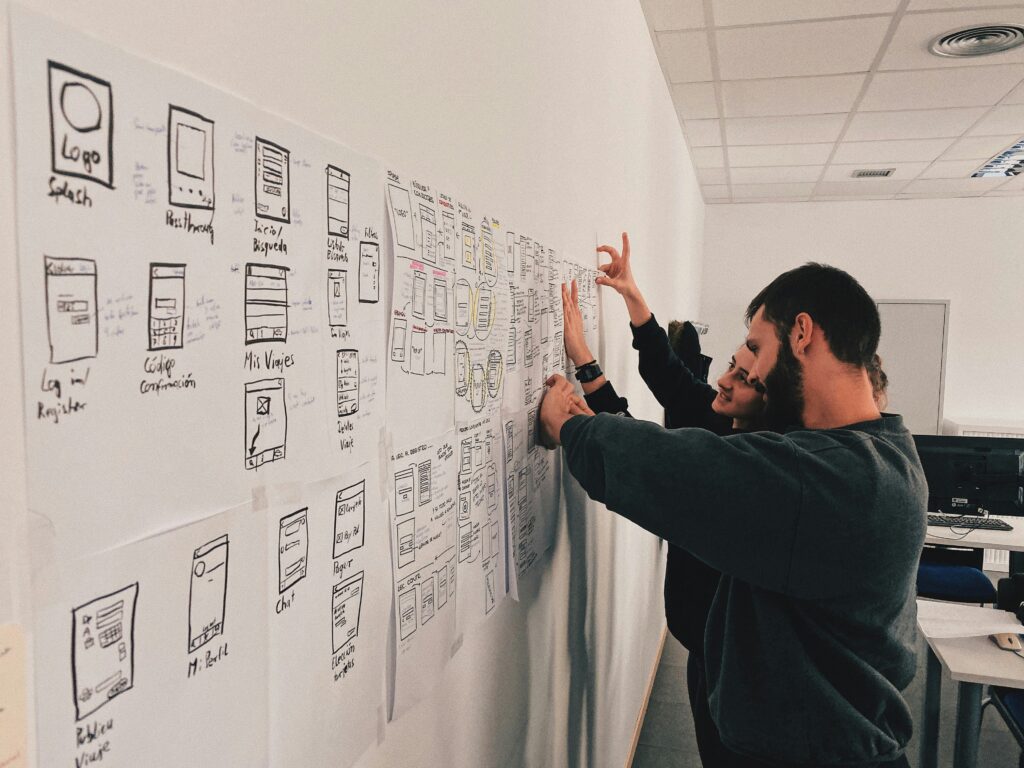 Design team arranging hand-drawn layout sketches on a studio wall to plan and sort production work