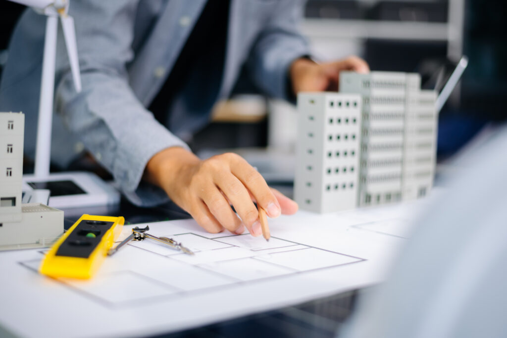 Architect marking up a floor plan beside building models while planning project staffing and production hours