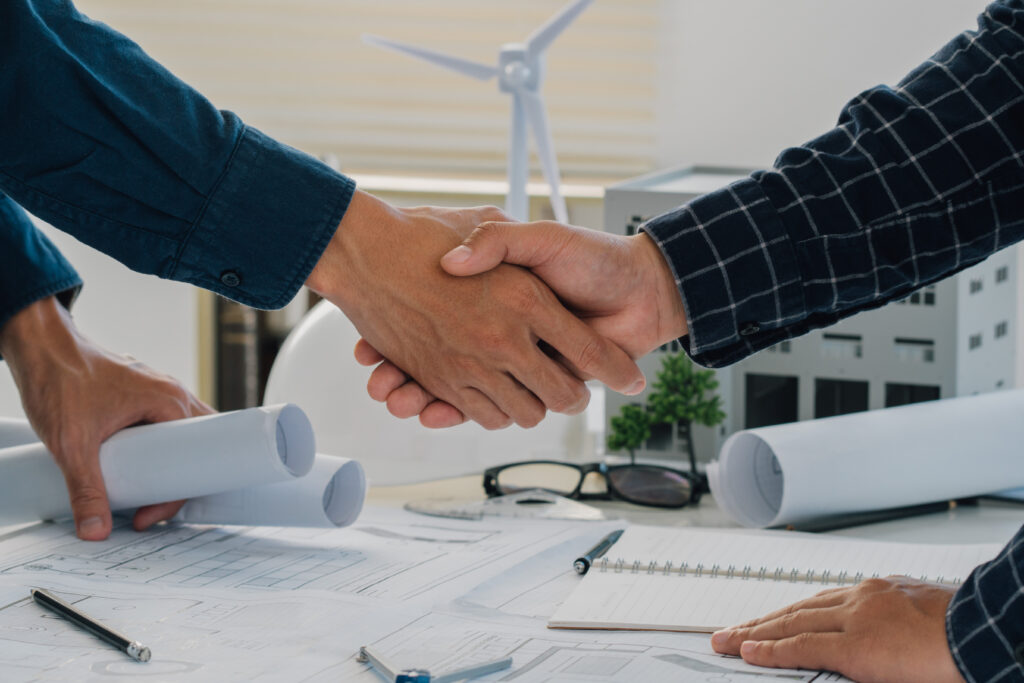 Architect and client shaking hands over blueprints after an architecture firm wins a new projec