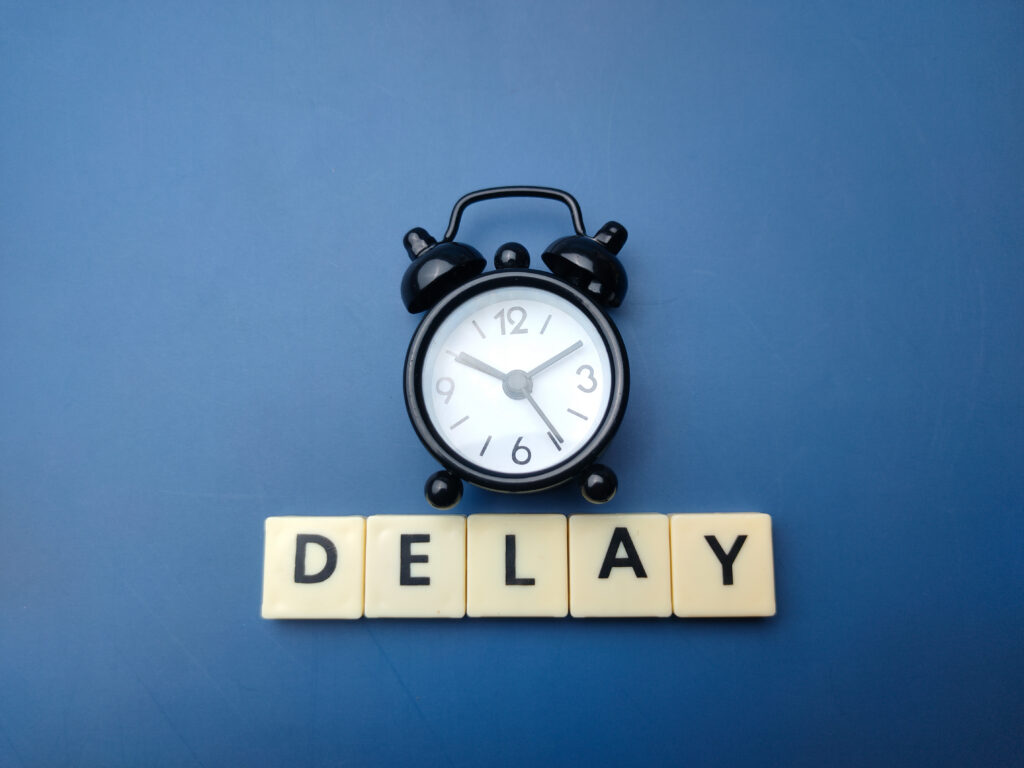 Alarm clock above letter tiles spelling “delay,” representing prior authorization delays in patient care