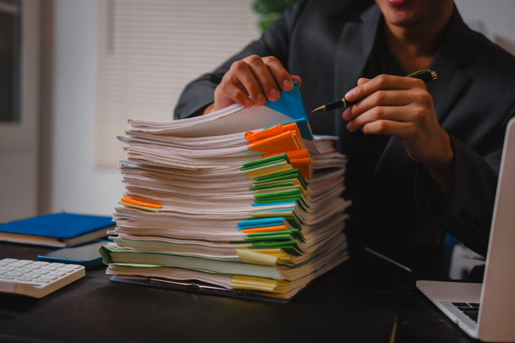 Tall stack of tabbed paperwork on a desk, showing how a prior authorization backlog builds up